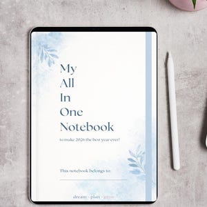 Pode incluir: Um caderno digital com o texto "My All In One Notebook" e a frase "to make 2026 the best year ever!" em um design de aquarela azul suave. Uma caneta branca está ao lado do caderno, com uma pequena planta em vaso no fundo.