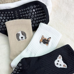 Könnte beinhalten: Eine Auswahl an Yoga-Socken in verschiedenen Farben, darunter Schwarz, Weiß und Beige. Jede Socke zeigt ein gesticktes Hunde- oder Katzengesicht. Die schwarzen Socken haben rutschfeste Griffe und den Text "YOGA S".