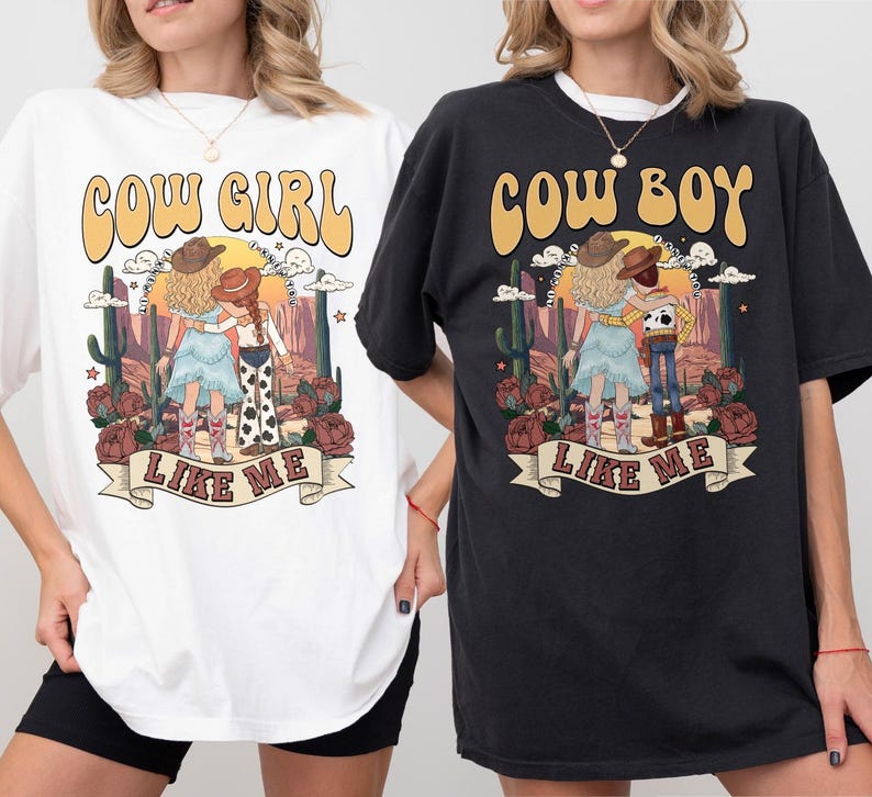 May include: A white t-shirt and a black t-shirt, each featuring a graphic print of a desert scene with cacti, roses, and two figures. The white shirt says COW GIRL LIKE ME, and the black shirt says COW BOY LIKE ME, both in a retro, curved font.