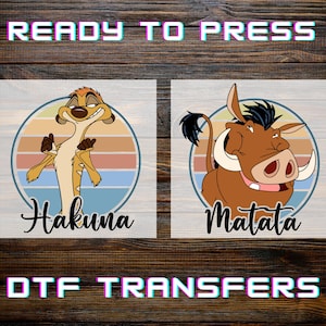 May include: Two DTF transfers featuring cartoon characters. One shows a meerkat with the word "Hakuna" below, and the other a warthog with "Matata". Both are set against a circular background with a sunset design. The text "READY TO PRESS" and "DTF TRANSFERS" are also visible.