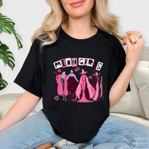 May include: Black t-shirt with the text "MEAN GIRLS" in white block letters and pink lipstick accents. The shirt features a cartoon illustration of four female characters in pink and purple outfits.