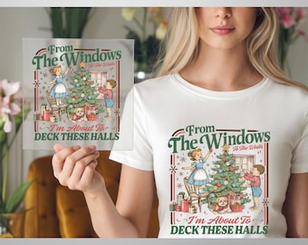May include: A white t-shirt featuring a vintage-style graphic of two children decorating a Christmas tree with a small dog nearby. The text reads From The Windows To The Walls I'm About To DECK THESE HALLS in green and red lettering.