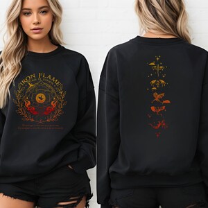 Op de afbeelding: Zwart sweatshirt met de tekst "IRON FLAMES TURN O DOWN" in goud en oranje. Het ontwerp aan de voorkant toont een cirkelvormig embleem met vlammen en een vogel. De achterkant heeft een verticaal ontwerp van gestileerde draken in tinten oranje en goud.