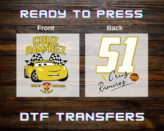 May include: A DTF transfer with a yellow race car design, displaying "Cruz Ramirez" and the number "51". The front shows the car, flags, and text. The back features the number and name. The words "READY TO PRESS" and "DTF TRANSFERS" are also visible.