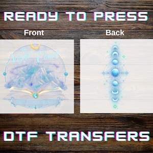 May include: Ready to press DTF transfers. The front design features a celestial mountain scene with the text "The Night Coast" and an open book. The back design shows a series of blue orbs and crescent shapes. The designs are in shades of blue and white.