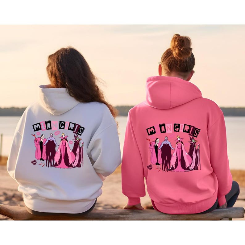 May include: Two hooded sweatshirts, one white and one pink, with a graphic on the back. The graphic features the text "MA GRILS" above a line of cartoon villain characters in pink and black. The sweatshirts are casual wear.