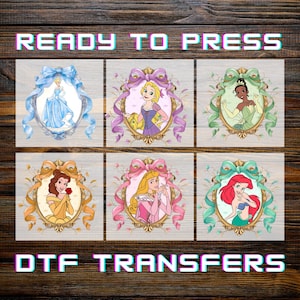 May include: Six DTF transfers featuring Disney princesses in ornate frames. Cinderella in a blue gown, Rapunzel in purple, Tiana in green, Belle in yellow, Aurora in pink, and Ariel with red hair. Text reads "READY TO PRESS" and "DTF TRANSFERS".