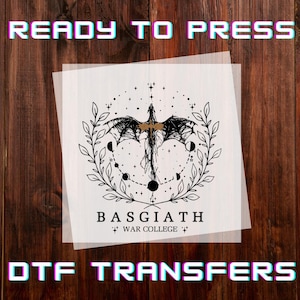 May include: A DTF transfer featuring a black dragon design with gold accents, surrounded by a wreath of leaves and moons. The text "BASGIATH WAR COLLEGE" is below the dragon. The words "READY TO PRESS" and "DTF TRANSFERS" are at the top and bottom.