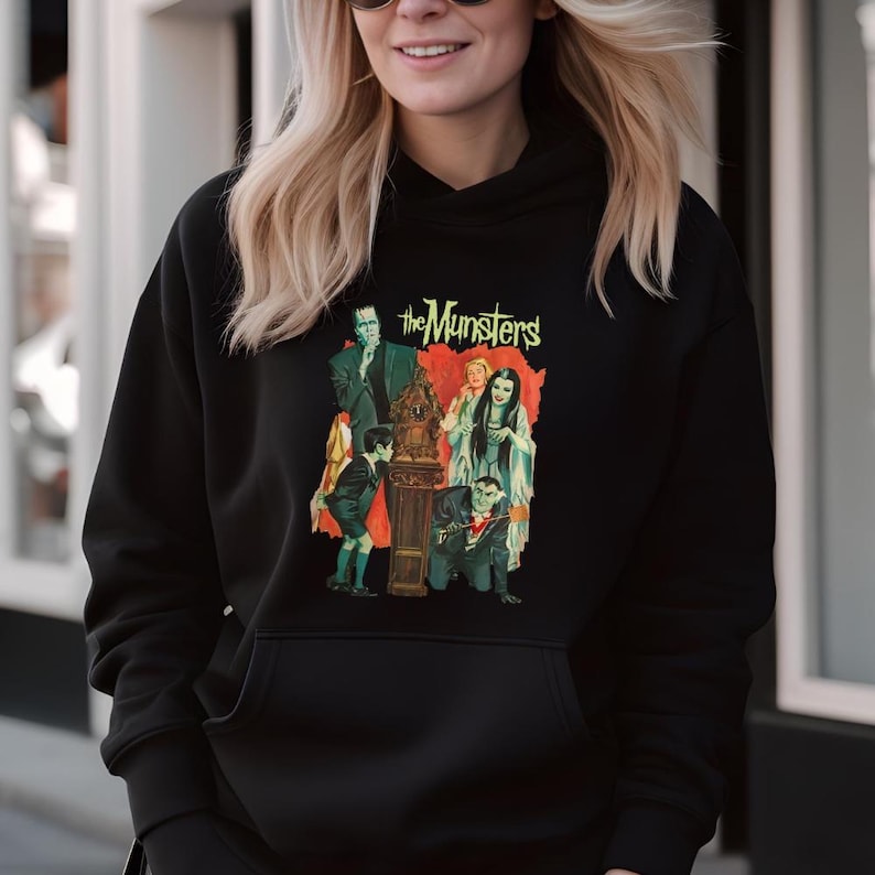 Peut inclure: Sweat-shirt &agrave; capuche noir avec un graphisme color&eacute; de la famille Munster. Le graphisme comprend les mots "the Munsters" en vert et des personnages de la s&eacute;rie t&eacute;l&eacute;vis&eacute;e classique. Le sweat-shirt a une poche avant et une capuche &agrave; cordon.