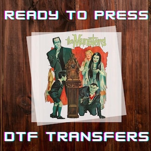 Peut inclure: Transfert DTF repr&eacute;sentant la famille Munster. L'image comprend Frankenstein, Lily Munster, Herman Munster et d'autres personnages. Les mots "READY TO PRESS" et "DTF TRANSFERS" sont affich&eacute;s dans une police r&eacute;tro.