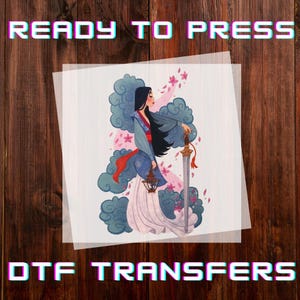 May include: DTF transfer featuring a stylized illustration of a woman in traditional attire, holding a sword. The design includes floral and cloud elements, with the text "READY TO PRESS" and "DTF TRANSFERS" in a pixelated font. The image is on a translucent sheet.