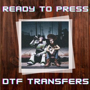 May include: DTF Transfers featuring a vintage-style image of Buzz Lightyear and Woody from Toy Story. The image shows the characters sitting together, with the text "READY TO PRESS" and "DTF TRANSFERS" in a retro font. The background is a wooden surface.