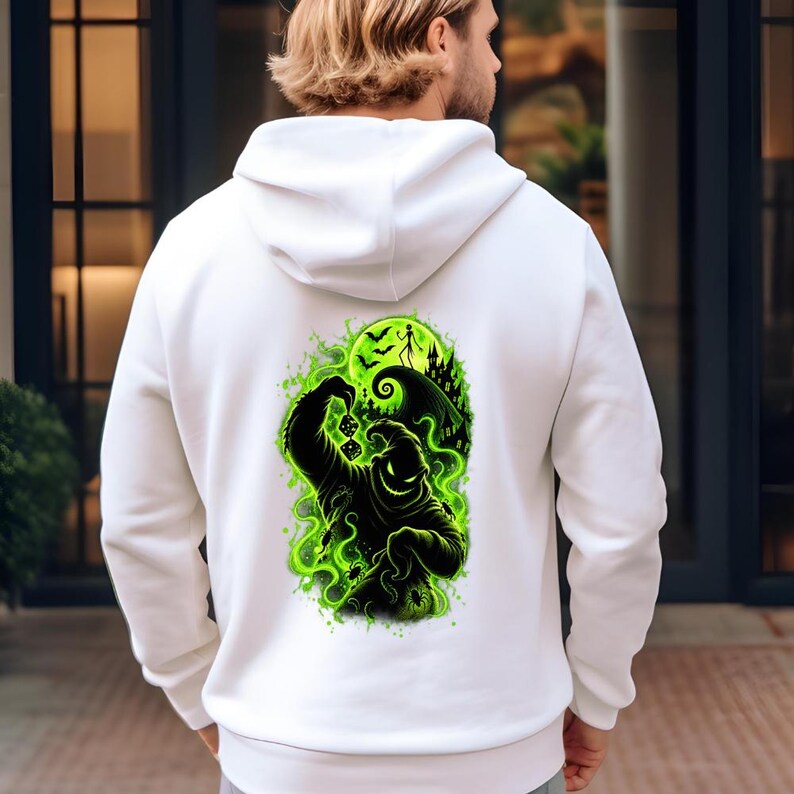 May include: A white hooded sweatshirt featuring a large graphic on the back. The design displays a black silhouette of a burlap sack character holding dice, surrounded by vibrant green smoke, bats, a crescent moon, and a dark hilltop castle.
