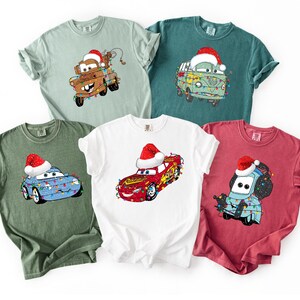 A collection of t-shirts featuring various cartoon car characters, including Cars, in festive holiday-themed designs.