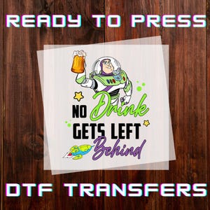 May include: A DTF transfer featuring Buzz Lightyear holding a beer mug, with the text "NO Drink GETS LEFT Behind". The design includes a star, a rocket, and the words "READY TO PRESS" and "DTF TRANSFERS".