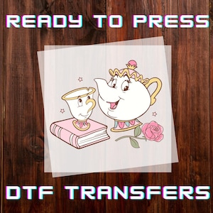 May include: DTF transfers featuring a cartoon image of Mrs. Potts and Chip from Beauty and the Beast. The image includes a pink rose, a book, and the text "READY TO PRESS" and "DTF TRANSFERS" in a colorful font. The background is a wooden surface.