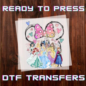 May include: DTF transfer featuring Disney princesses, a pink polka-dot bow, and the text "READY TO PRESS". The image includes a castle and Mickey Mouse-themed elements, set against a wooden background. The words "DTF TRANSFERS" are also displayed.