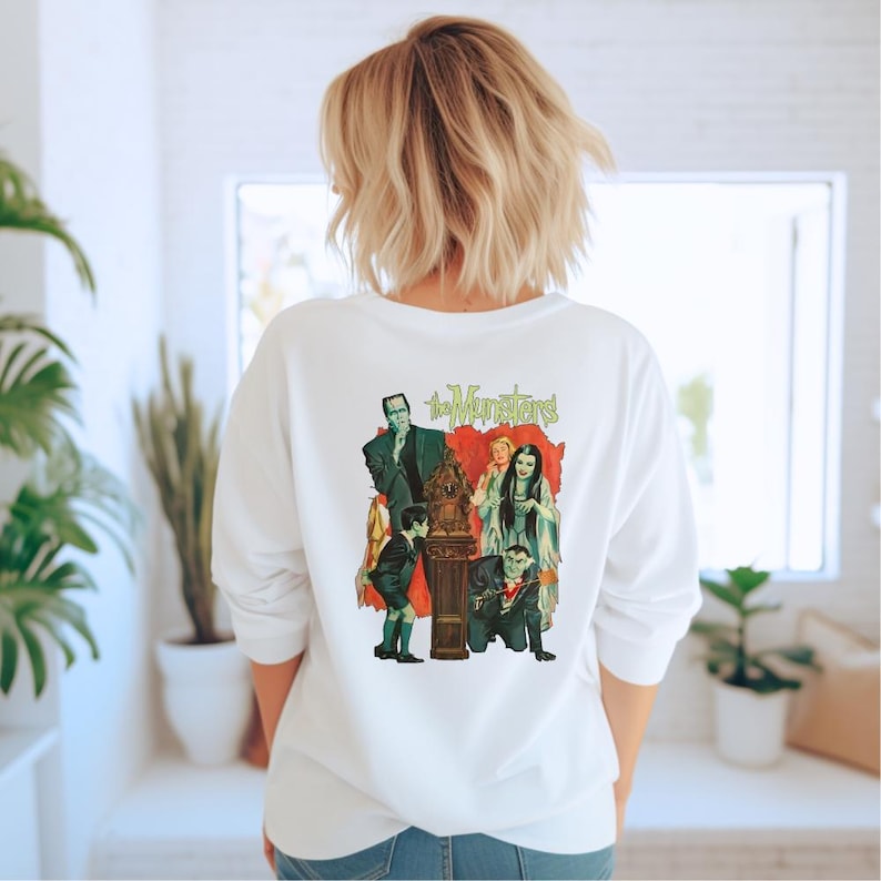 Peut inclure: Sweat-shirt blanc &agrave; manches longues avec un graphisme color&eacute; des Munsters. Le motif pr&eacute;sente les personnages de la s&eacute;rie t&eacute;l&eacute;vis&eacute;e classique, avec le titre de l'&eacute;mission en vert. Le sweat-shirt est de style d&eacute;contract&eacute; et confortable.