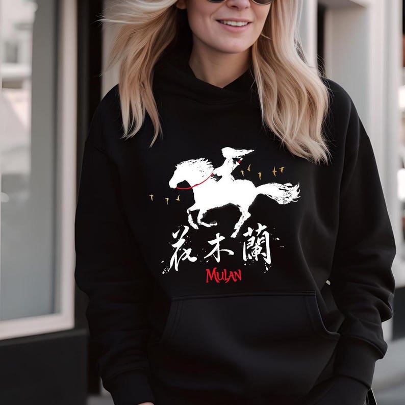 Pode incluir: Moletom preto com um gr&aacute;fico branco de uma pessoa montando um cavalo, caracteres chineses e a palavra "Mulan" em vermelho. O design inclui p&aacute;ssaros em voo. Um moletom confort&aacute;vel e cl&aacute;ssico.