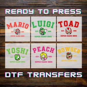 May include: Six DTF transfer designs featuring Super Mario Bros characters: Mario, Luigi, Toad, Yoshi, Peach, and Bowser. Each design includes the character's name, a graphic, and the text "EST. 1985 SUPER MARIO BROS." The words "READY TO PRESS" and "DTF TRANSFERS" are also displayed.