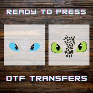 May include: Two DTF transfer designs featuring dragon eyes. One design has light blue eyes with black pupils, and the other has green eyes with black spots. The text "READY TO PRESS" and "DTF TRANSFERS" are displayed in a colorful, glitch-style font.