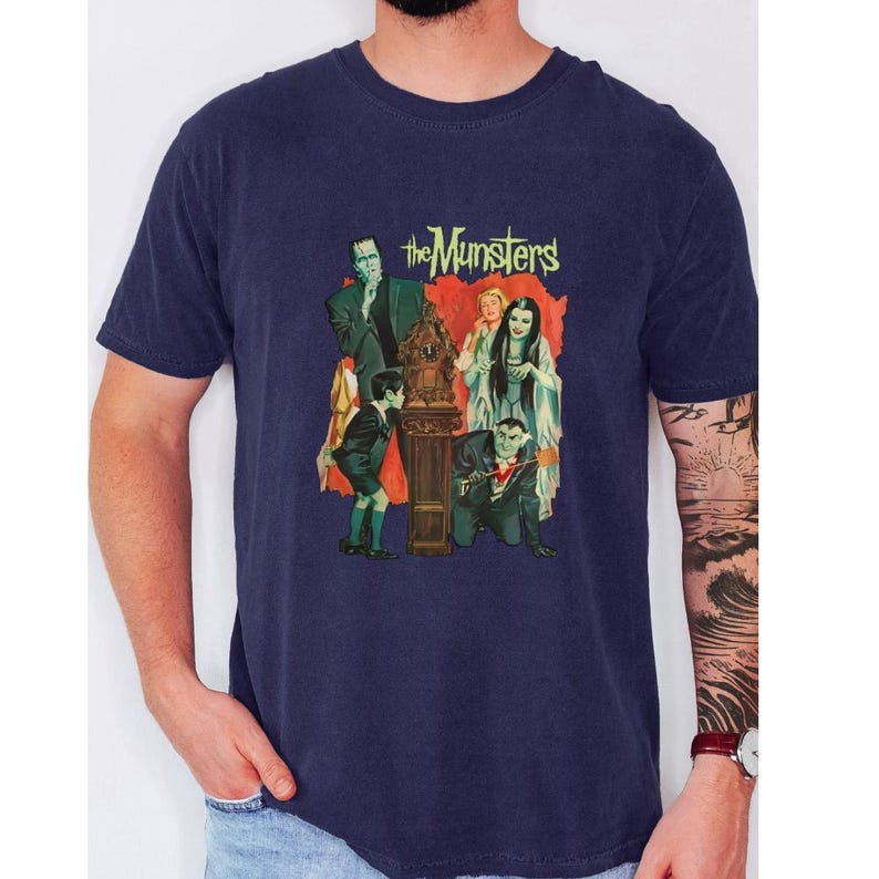 Peut inclure: T-shirt bleu marine avec un graphisme vintage de la famille Munster. L'image comprend Frankenstein, Lily Munster, Herman Munster et d'autres personnages de la s&eacute;rie t&eacute;l&eacute;vis&eacute;e classique. Le texte "The Munsters" est affich&eacute; en jaune.