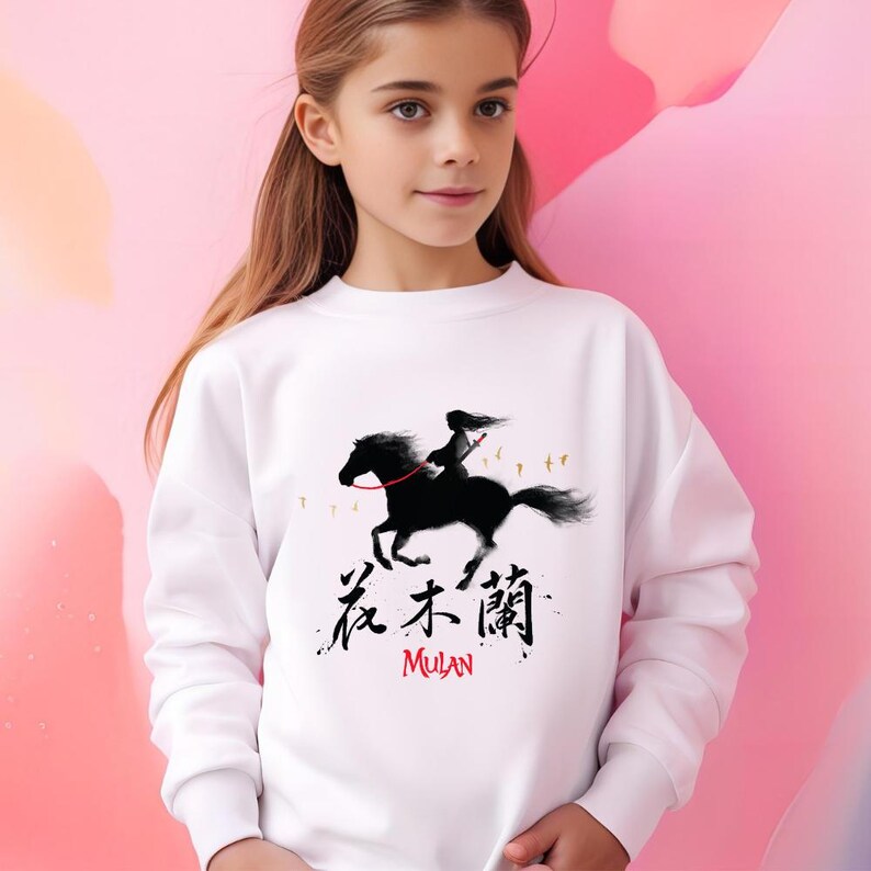 Pode incluir: Camisola branca com uma ilustra&ccedil;&atilde;o preta de uma pessoa a cavalo. O design inclui caracteres chineses e a palavra "Mulan" em vermelho. A obra de arte &eacute; uma representa&ccedil;&atilde;o estilizada.