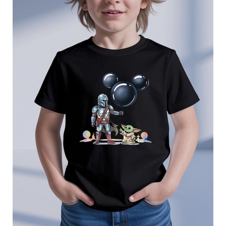 May include: Black t-shirt featuring a graphic of The Mandalorian, Baby Yoda, and three black Mickey Mouse-shaped bubbles. The characters are set against a colorful, rainbow-like background.