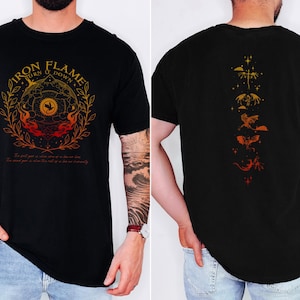 Op de afbeelding: Zwart t-shirt met een grafische voorkant met de tekst "IRON FLAME" in goud en oranje, rond een cirkelvormig ontwerp met vlammen. De achterkant van het shirt toont een verticale reeks drakenillustraties in oranje en goud.
