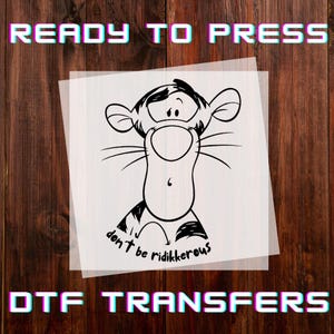 May include: A DTF transfer featuring a black and white cartoon tiger with the text "don't be ridikkerous". The words "READY TO PRESS" and "DTF TRANSFERS" are in a colorful, 3D font.