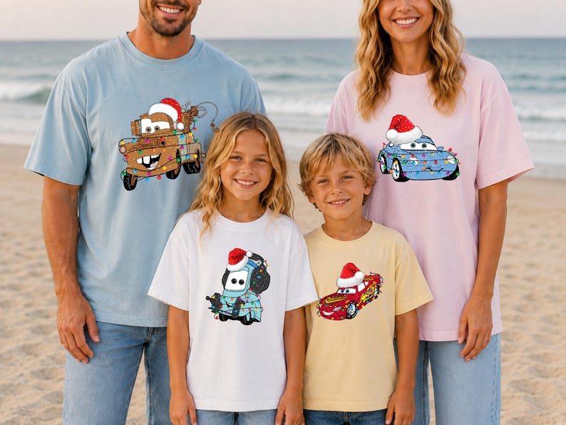 A family of four, consisting of two adults and two children, are standing on a beach wearing matching t-shirts with cartoon characters from the Cars movie.