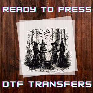 May include: A black and white DTF transfer sheet featuring a detailed illustration of four witches in pointed hats standing in a forest around a bubbling cauldron, with bats flying overhead. The text READY TO PRESS DTF TRANSFERS is visible.