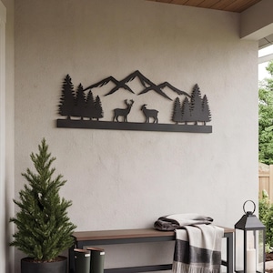 May include: A black metal wall art piece featuring a silhouette of a mountain range, pine trees, a deer, and a goat. The horizontal design is mounted on a light-colored wall above a wooden bench, creating a nature-inspired decorative display.