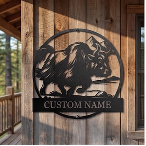 Op de afbeelding: Een rond wandbord van zwart metaal met een silhouet van een jak in profiel en bergtoppen op de achtergrond. Het ontwerp bevat een horizontale rechthoekige balk aan de onderkant met de tekst CUSTOM NAME in hoofdletters.