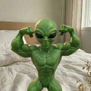 May include: A green alien figurine flexing its arms, showcasing its muscular physique. The alien has large black eyes and is posed in a confident stance. The figurine is a vibrant green color.