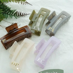 May include: Five rectangular hair claw clips in shades of brown, olive green, grey, off-white, and lavender. Each clip has gold initials. The image includes the text "Customize Your Initials~."