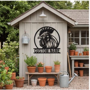 May include: A black metal wall sign featuring a circular frame with a rooster head silhouette and the text CUSTOM NAME centered at the bottom. The sign is mounted on the exterior wall of a light gray shed surrounded by various potted plants.
