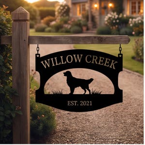 May include: A black metal hanging sign suspended from a wooden post. The sign features the text WILLOW CREEK at the top, a silhouette of a dog standing in grass in the center, and the text EST. 2021 at the bottom, all in a clean, bold font.