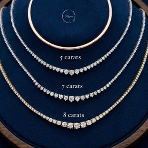 May include: Three tennis necklaces with round brilliant cut stones arranged in a row. The necklaces are labeled 5 carats, 7 carats, and 8 carats. A circular logo with the text Kaya Joy is positioned at the top center above the necklaces.