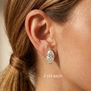 May include: A marquise-cut diamond stud earring set in a metallic prong setting, worn on an earlobe. The text 2 cts each is visible below the earring, indicating the weight of the stone in carats for each individual piece of jewellery.