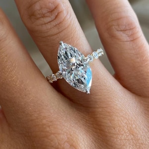 Op de afbeelding: Een ring met een marquise-geslepen diamant met een grote, langwerpige centrale steen in een metalen band. De band is aan de zijkanten versierd met een reeks kleinere, rondgeslepen diamanten, wat zorgt voor een continu sprankelend effect.