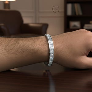 May include: A silver bracelet with rectangular, clear stones. The bracelet is worn on a person's wrist, and the stones reflect light. The bracelet is a piece of jewelry.