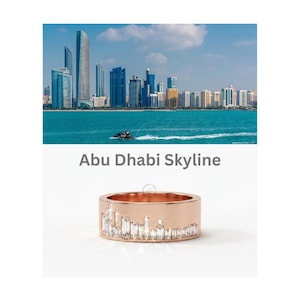 May include: A rose gold band ring featuring a series of baguette-cut clear stones arranged along the lower edge to mimic the Abu Dhabi skyline. The text Abu Dhabi Skyline is printed above the ring, which sits below a photo of the city skyline.