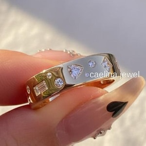 Könnte beinhalten: Ein goldfarbener Ring mit einer Reihe von eingebetteten Edelsteinen in verschiedenen Formen, darunter rund, Baguette und dreieckig. Der Ring hat eine polierte Oberfläche und der Text "caelina jewel" ist sichtbar.