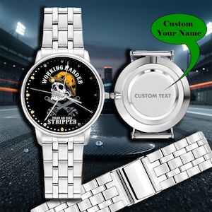May include: Silver wristwatch with a black watch face featuring a skull wearing a yellow hard hat and crossed wrenches. The watch face has the text "WORKING HARDER THAN AN UGLY STRIPPER". The back of the watch has space for custom text.