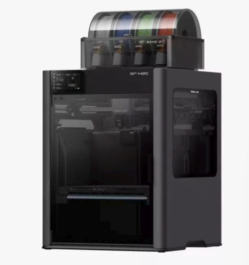 May include: A black 3D printer with a clear front panel and a filament storage unit on top. The storage unit contains multiple spools of filament in various colors. The printer has the text "S H2C" on the front.