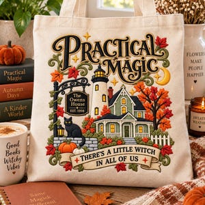 May include: A cream-colored canvas tote bag featuring an embroidered design of a house, a lighthouse, a black cat, and autumn leaves. The text reads Practical Magic, The Owens House Est. 1998, and There's a Little Witch in All of Us.