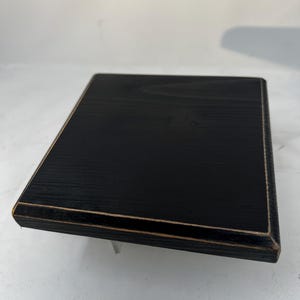 May include: Black square wooden coaster with a light brown border.