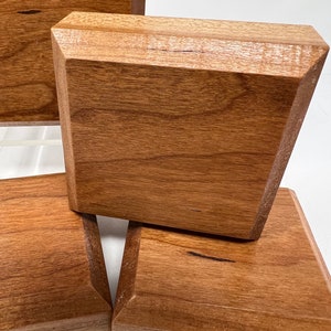 May include: Four wooden square coasters with beveled edges. The coasters are made of light brown wood with a natural grain pattern.