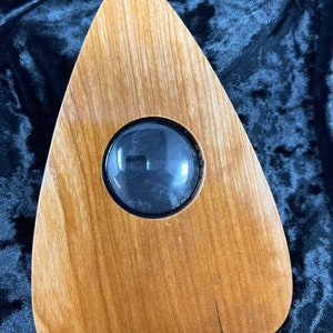 May include: A wooden Ouija board with a round, black glass window in the center.